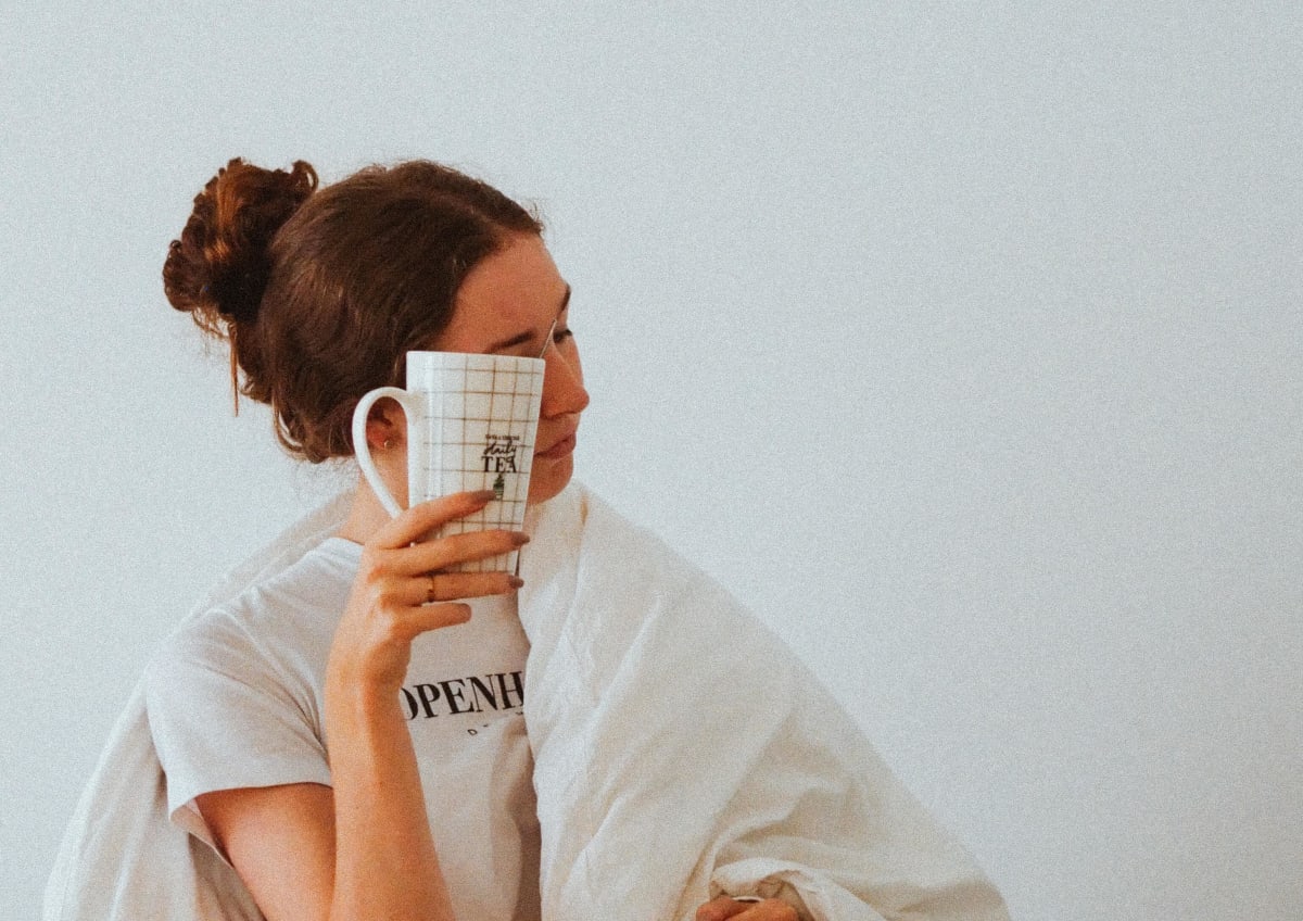 Jeune femme présentant des symtomes de fatigue, enveloppée dans une couverture et tenant un mug