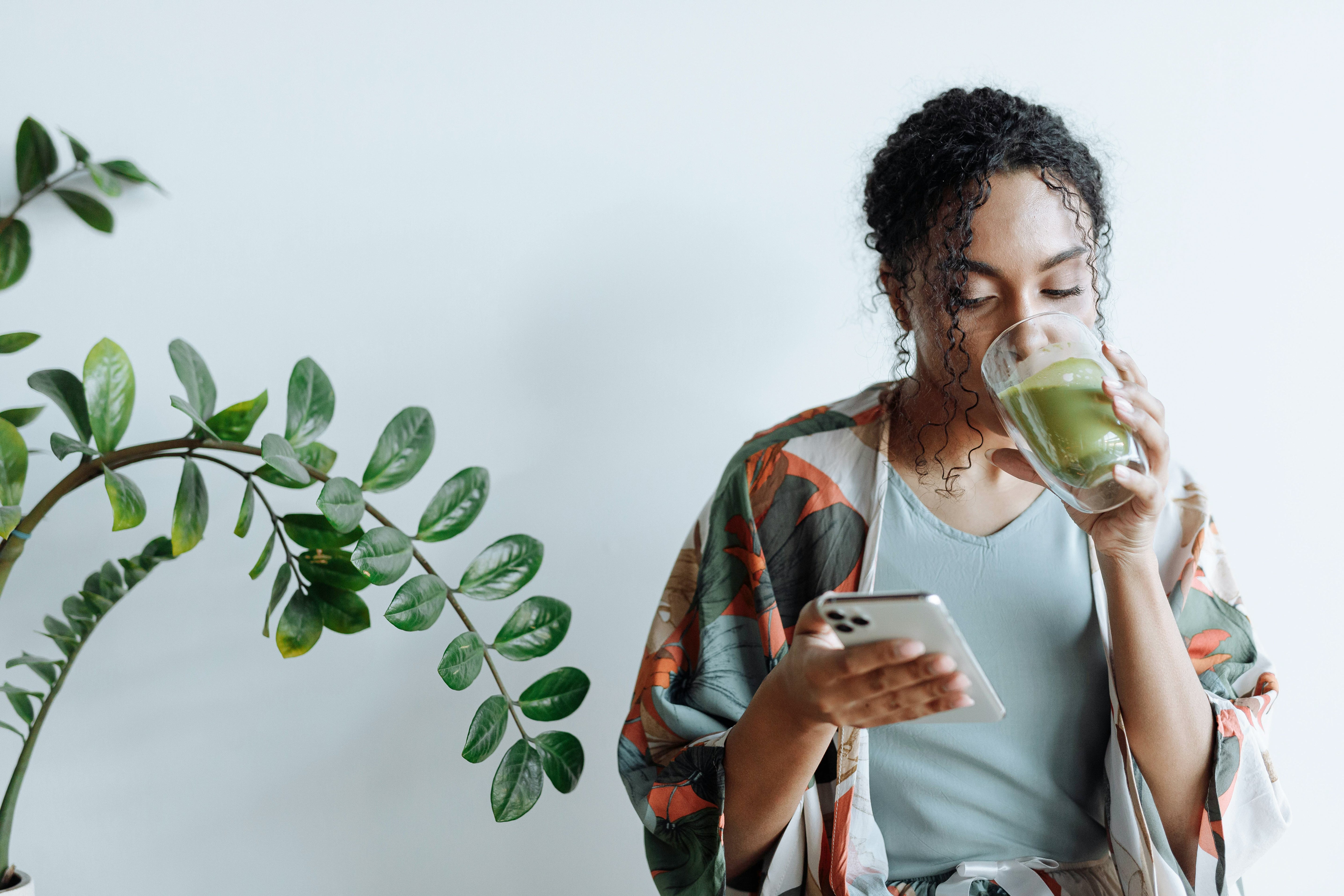 Une jeune femme buvant du thé matcha en regardant son smartphone