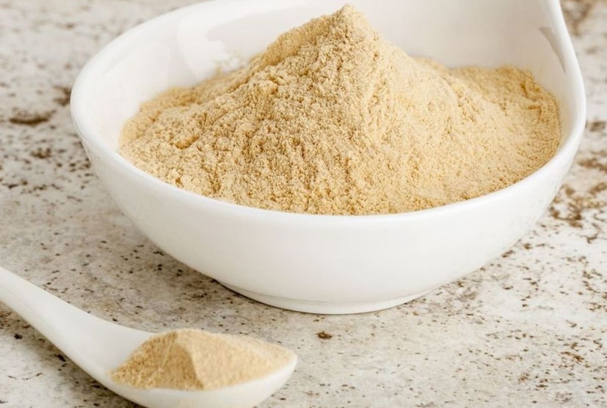 Gros plan sur un bol de maca avec une cuillère pleine de maca en poudre