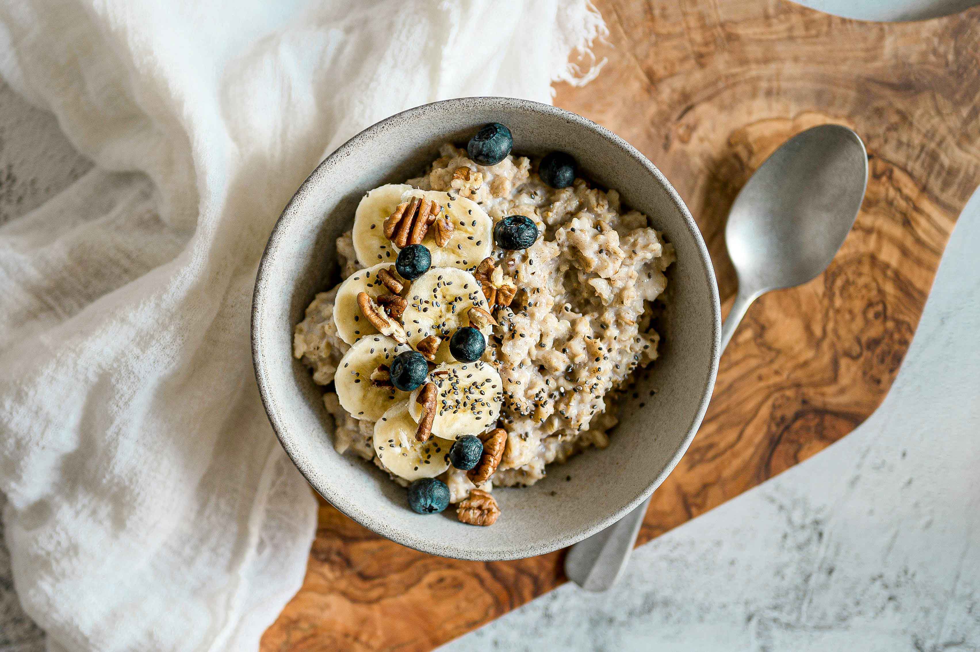 Bol de porridge protéiné avec des tranches de banane, des myrtilles et des noix de pécan