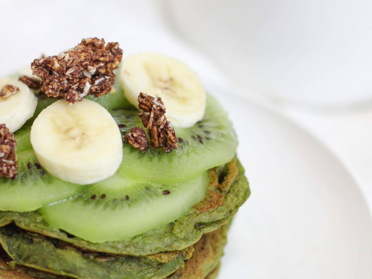 Pile de pancakes verts au matcha et à la banane, avec des tranches de banane et du granola en topping