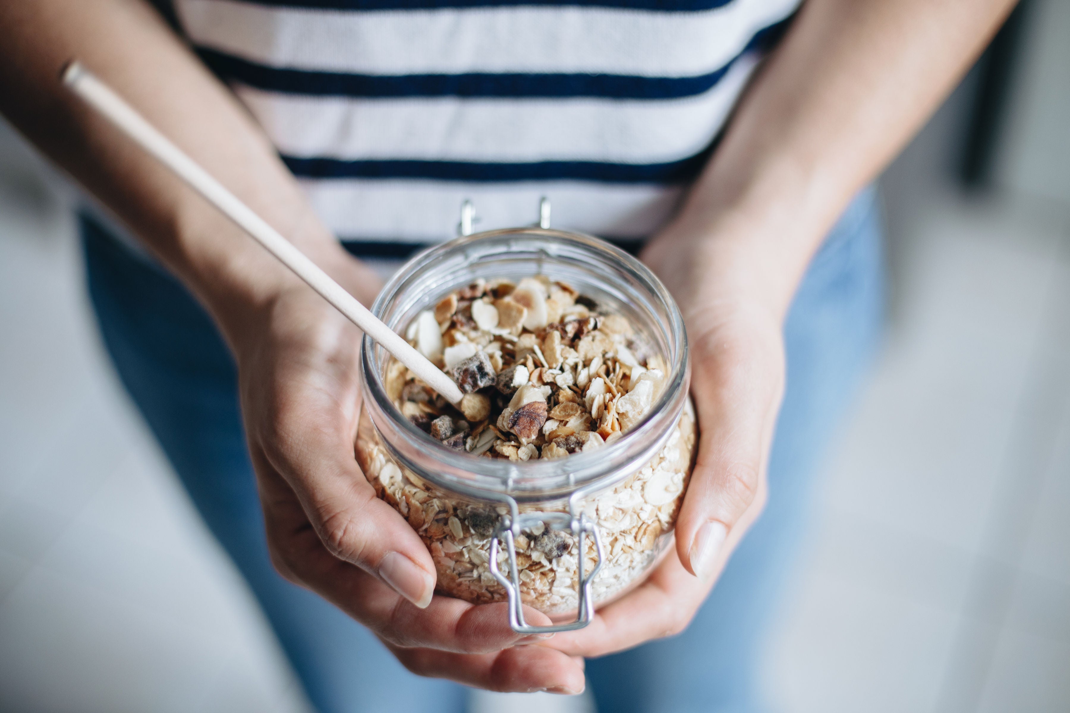 Un muesli bowl dans un pot en verre, avec une cuillère en bois, tenue par deux mains