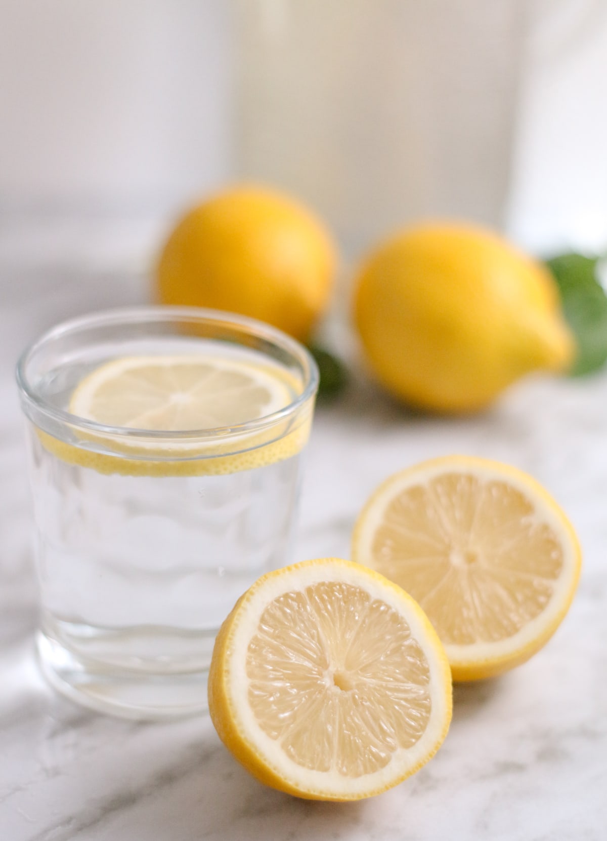 Verre d'eau avec une tranche de citron pour le petit-déjeuner, à côté de citrons entiers et d'un citron coupé en deux