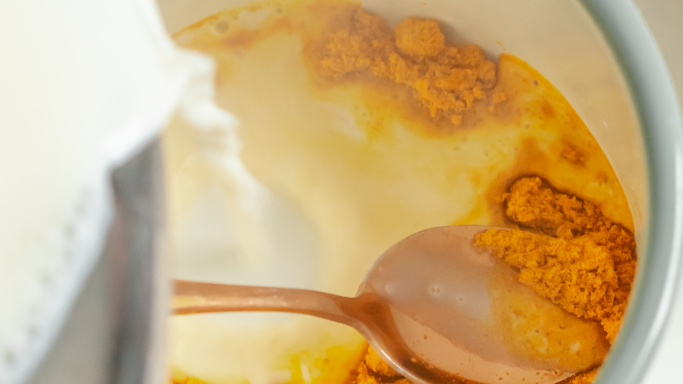Tasse de lait d'or avec le mélange d'épices au fond et du lait chaud versé depuis une casserole