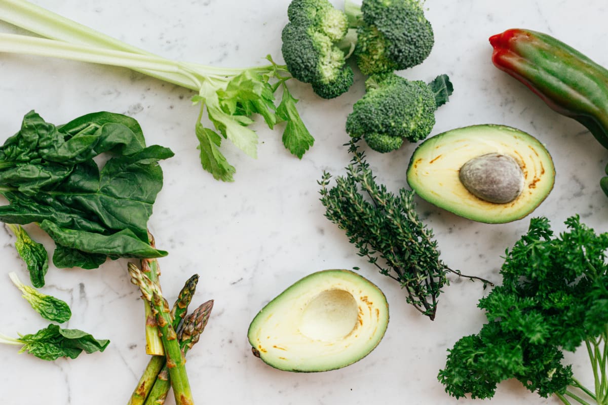 Aliments anti fatigue sur une table : un avocat, du brocoli, des brins d'asperge et des feuilles d'épinard