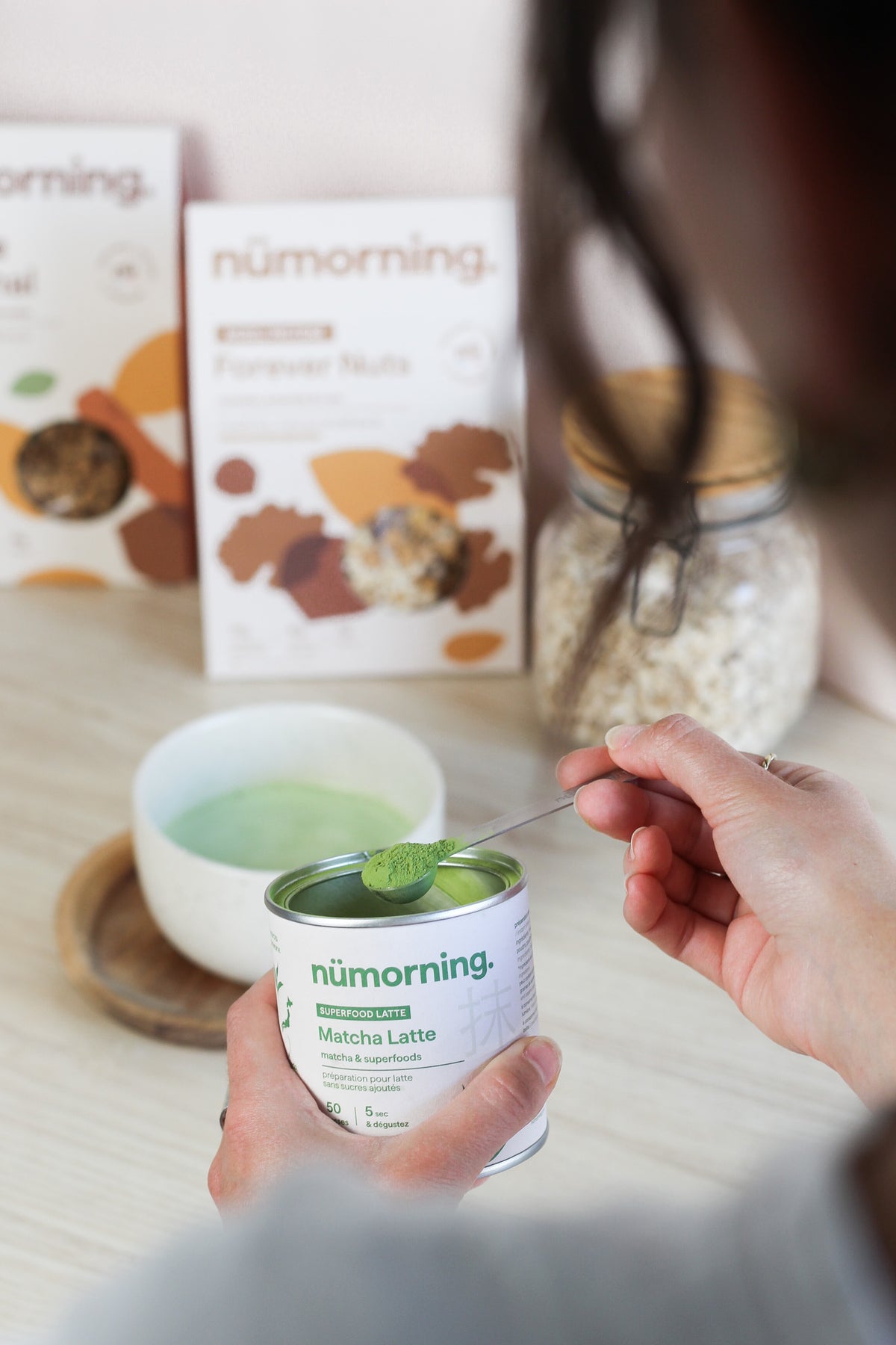Une jeune femme verse une cuillère de préparation pour matcha latte dans son bol