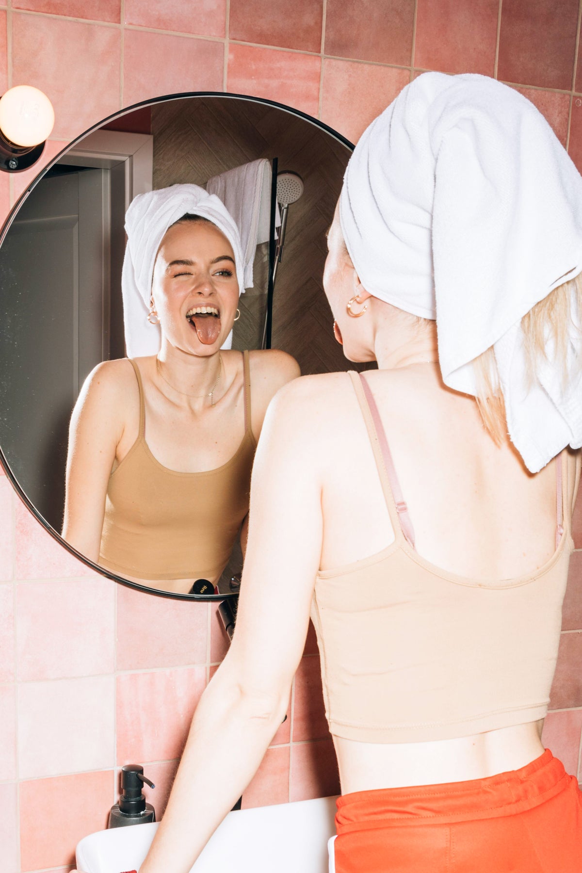 Jeune femme souriante après sa routine de soin, peau fraîche et lumineuse devant le miroir
