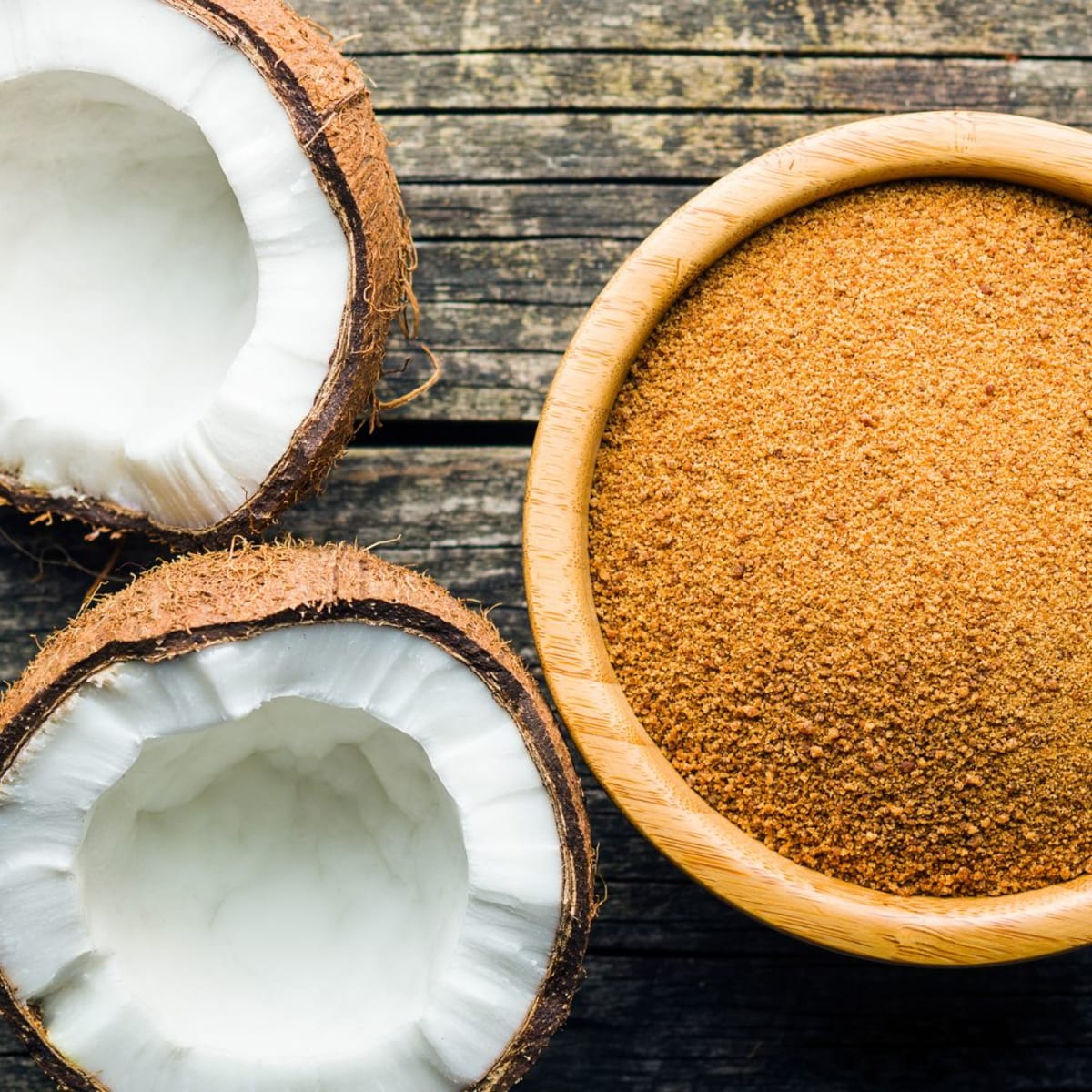 Bol de sucre de coco à côté d'une noix de coco ouverte en deux parties