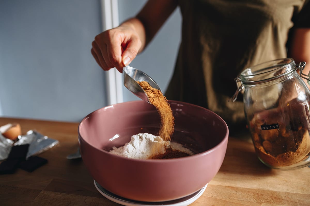 Jeune femme en train de patisser et de verser du sucre de coco dans un saladier avec de la farine