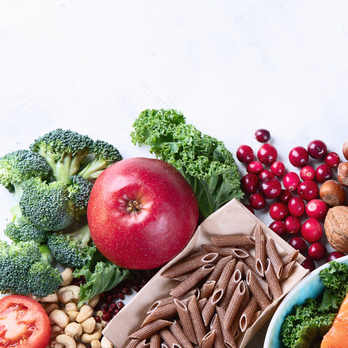 Exemples d'aliments riches en fibres sur une table, avec une pomme, des pâtes complètes, des brocolis et des noix de cajou