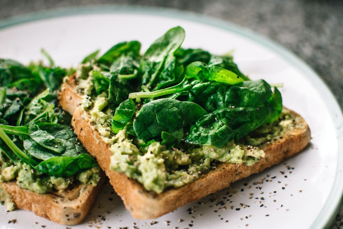 Deux tartines de pain grillé avec des aliments anti fatigue comme l'avocat et des épinards dans une assiette