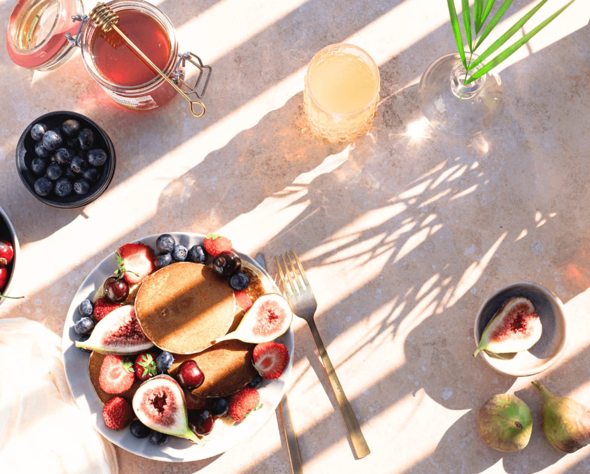 Assiette de pancakes avec des fruits frais et du miel comme exemple de quoi manger au petit-déjeuner