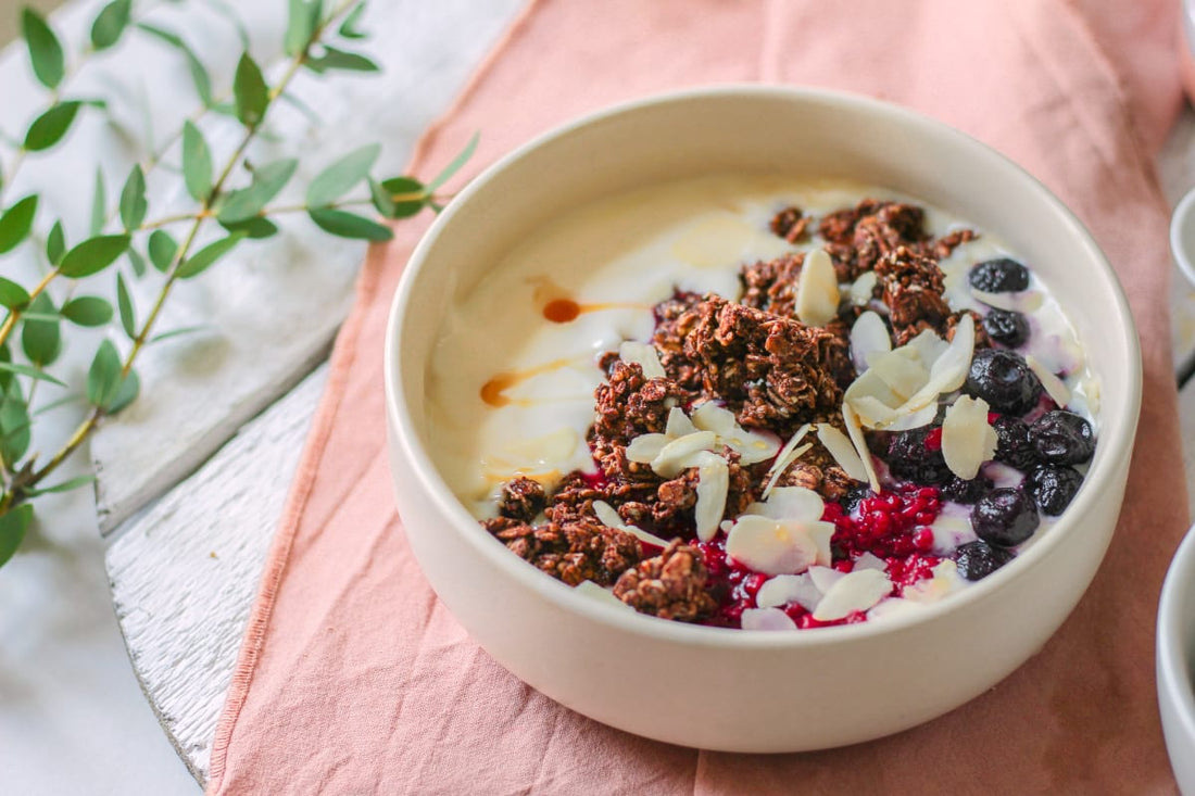 Granola bowl avec des amandes effilées et des fruits rouges en topping sur une table en bois gris