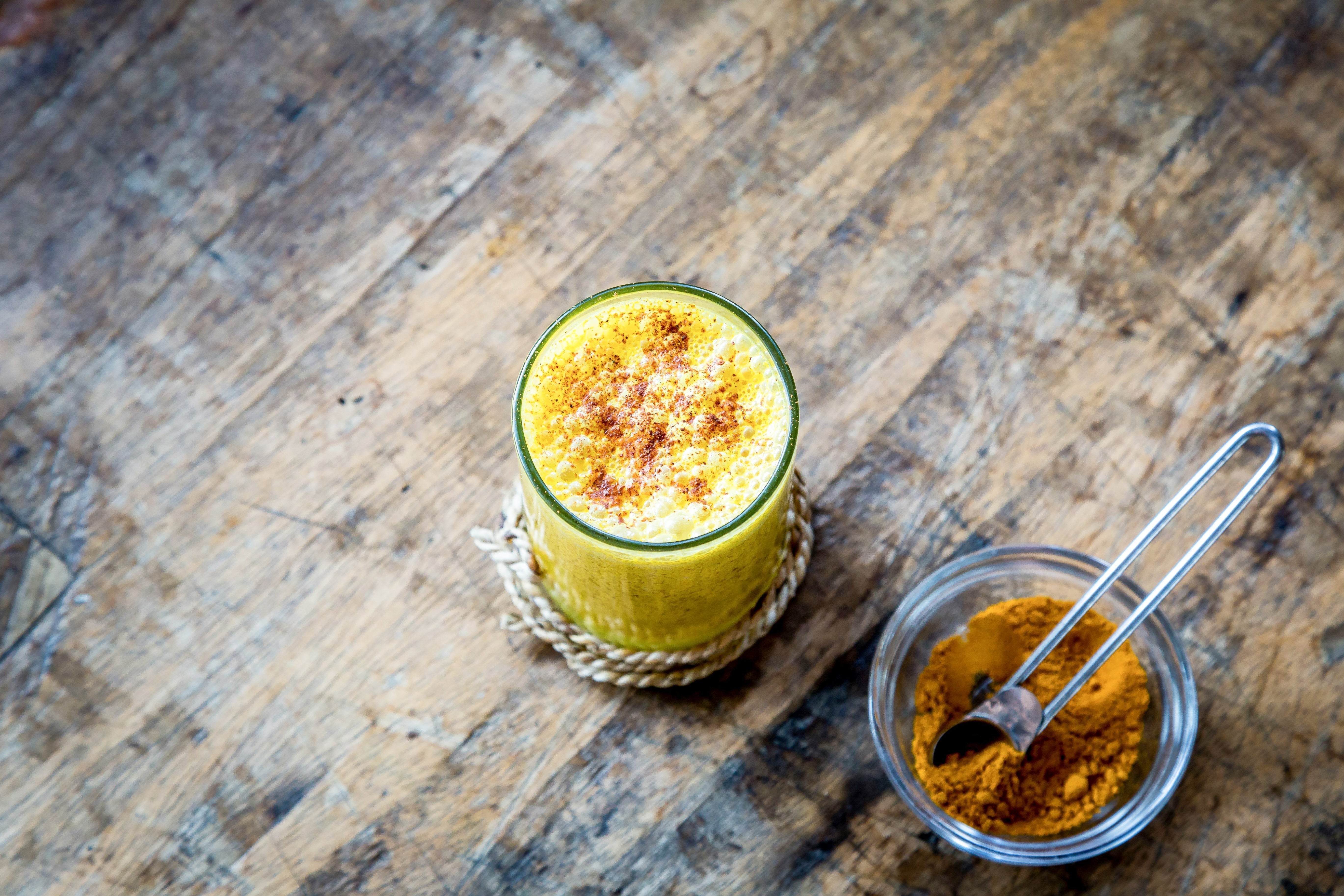 Gros plan sur un verre de golden latte avec une coupelle de curcuma en poudre à côté