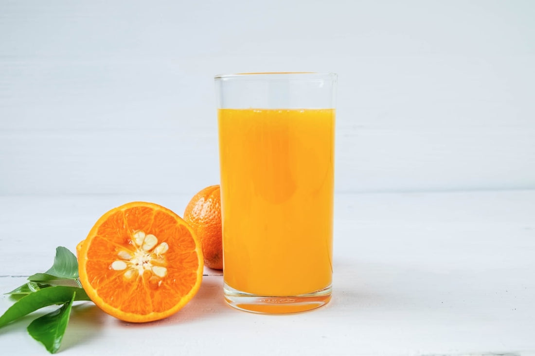 Un grand verre de jus d'orange pour le matin, à côté d'une orange coupée en deux