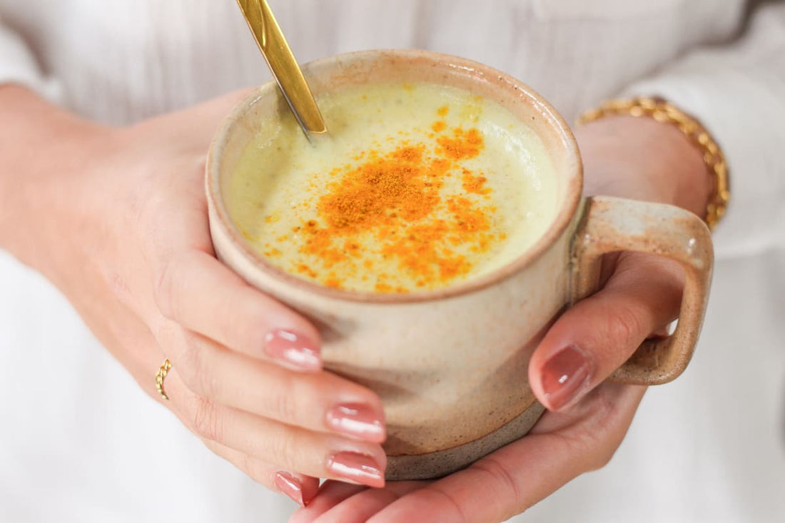 Tasse de lait d'or ou golden latte maison avec une cuillère, dans les mains d'une jeune femme