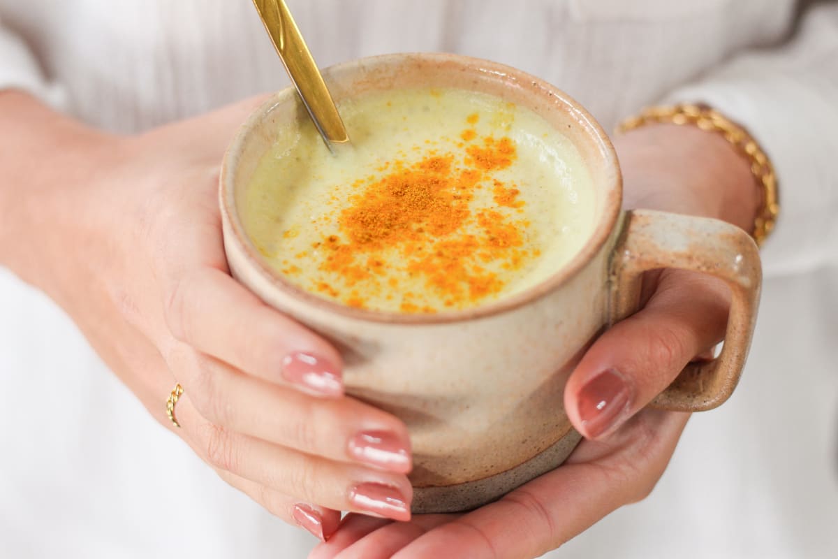 Tasse de lait d'or ou golden latte maison avec une cuillère, dans les mains d'une jeune femme