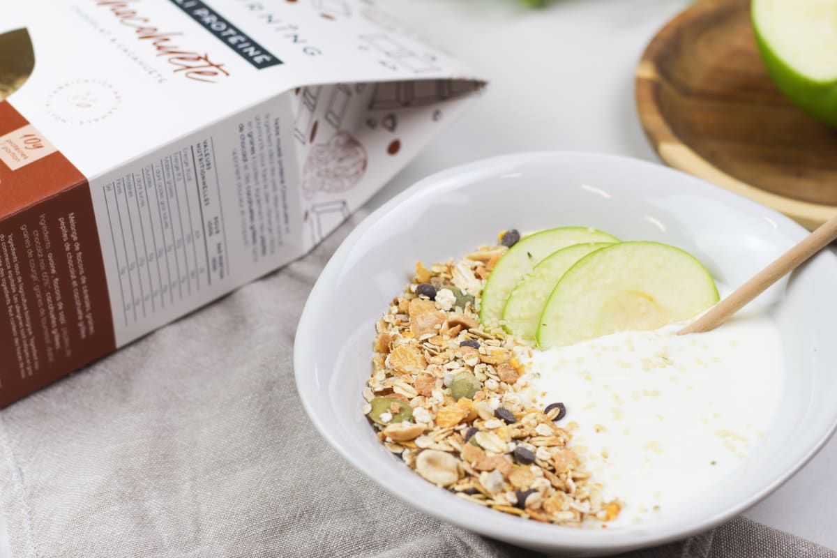 Bol de muesli sur base yaourt avec des tranches de pommes vertes et une cuillère en bois