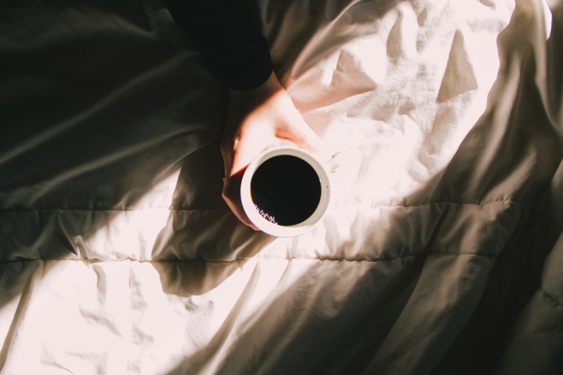 Mug de café tenu par une femme sur un lit avec la lumière du jour, en plein rituel matinal