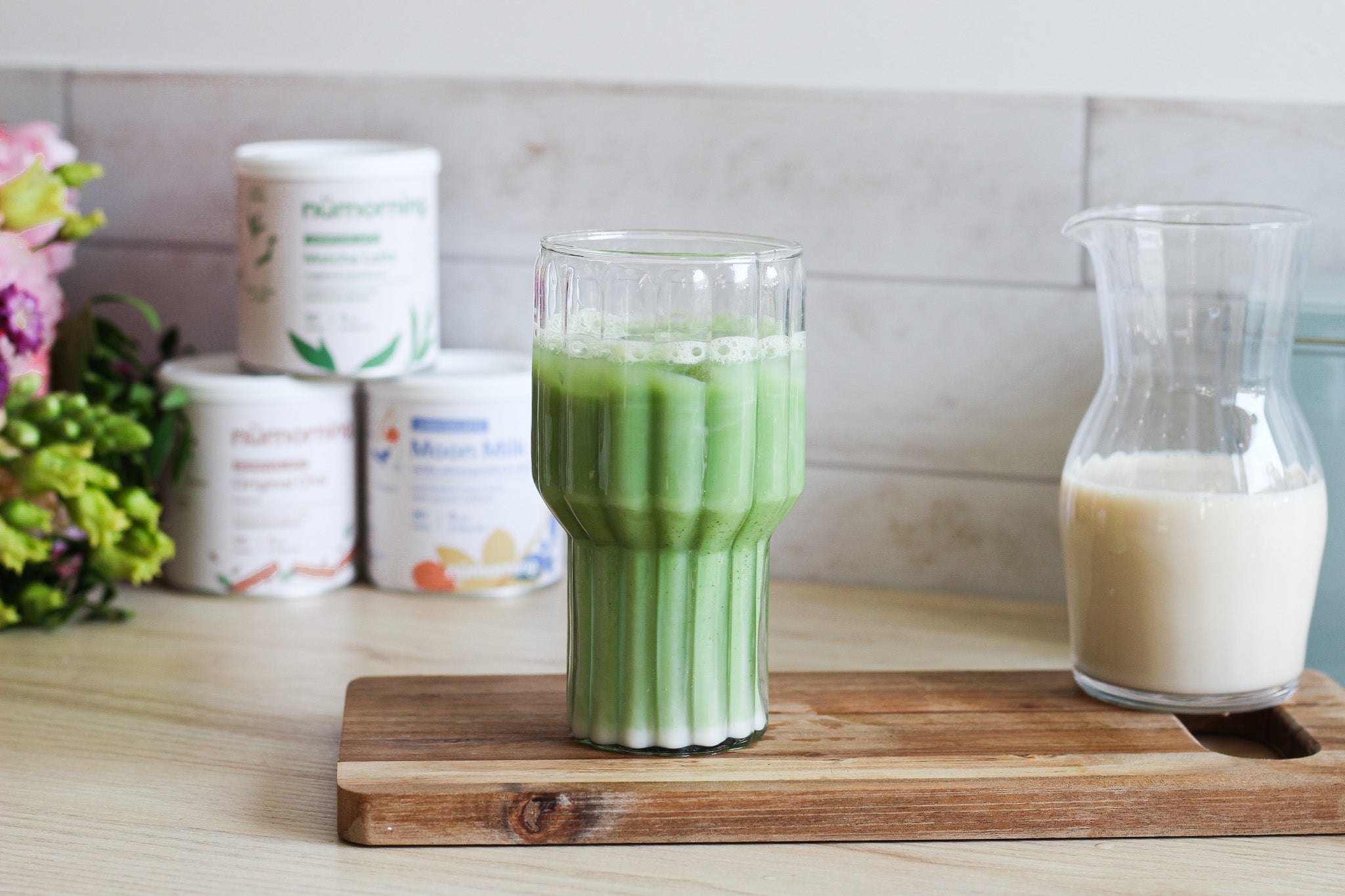 Verre de matcha latte glacé avec une carafe de lait végétal sur le côté