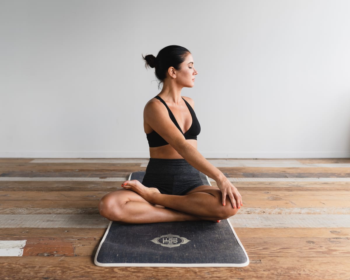 Jeune femme sur un tapis de yoga, assise en tailleur et faisant une torsion de la colonne vertébrale