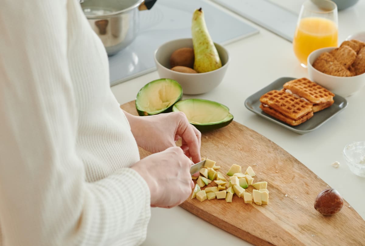 Jeune femme découpant un avocat en petits morceaux sur une planche à découper Image