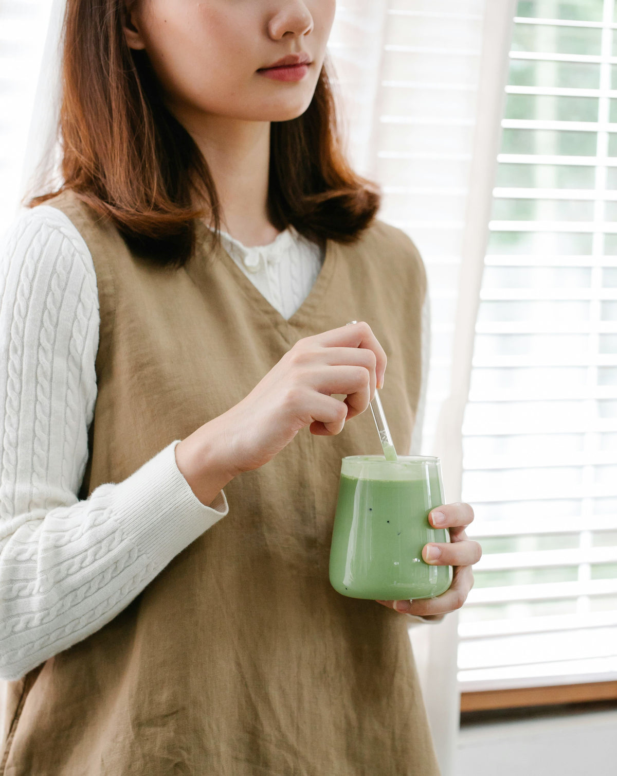 Une jeune femme tient un verre de matcha latte dans les mains