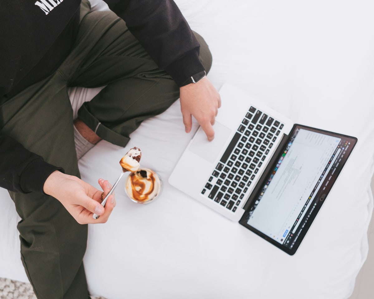 Jeune homme travaillant sur son ordinateur portable, en train de manger une collation sucrée à la cuillère