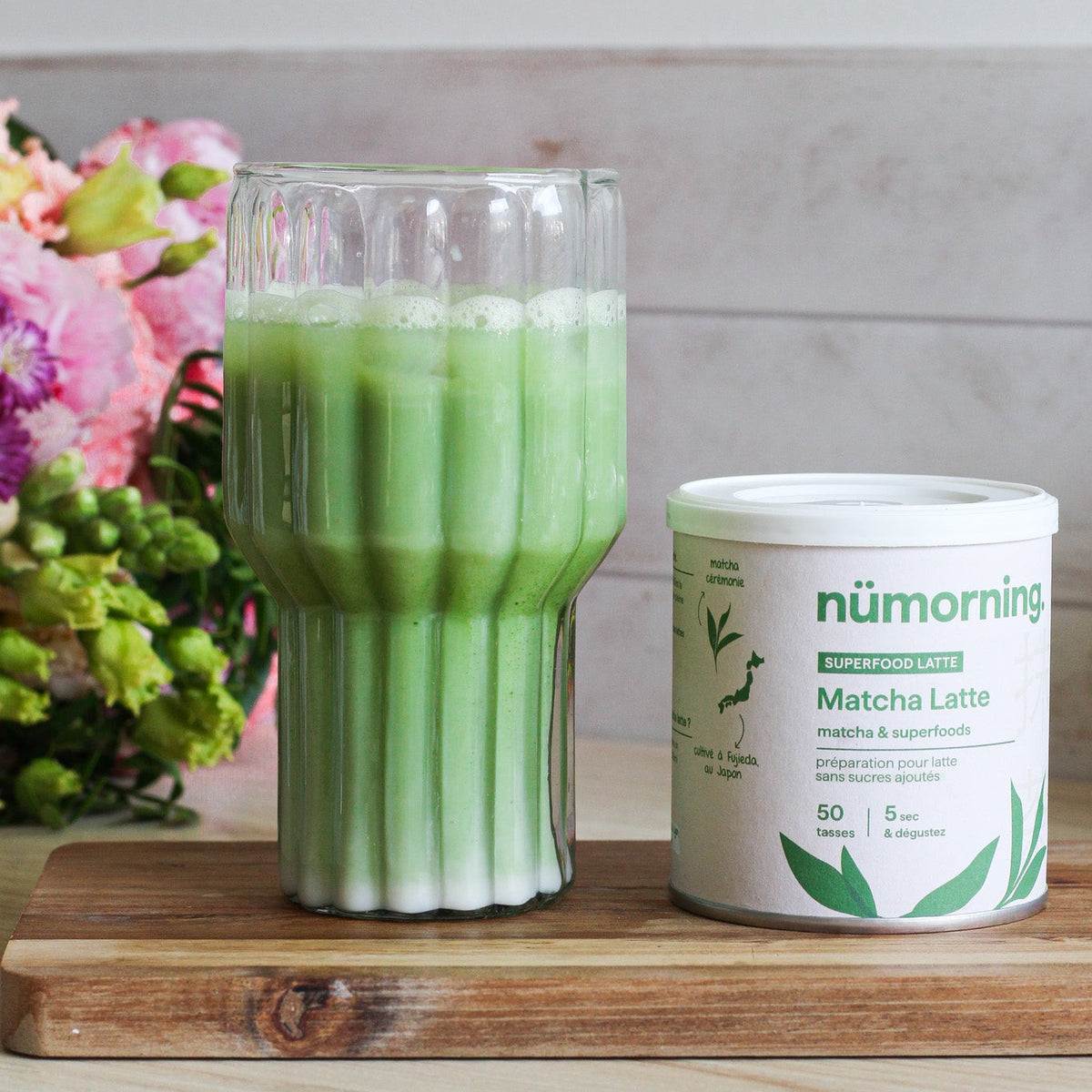 Verre de matcha latte bio préparé avec le mélange en poudre de nümorning, à côté de la boite