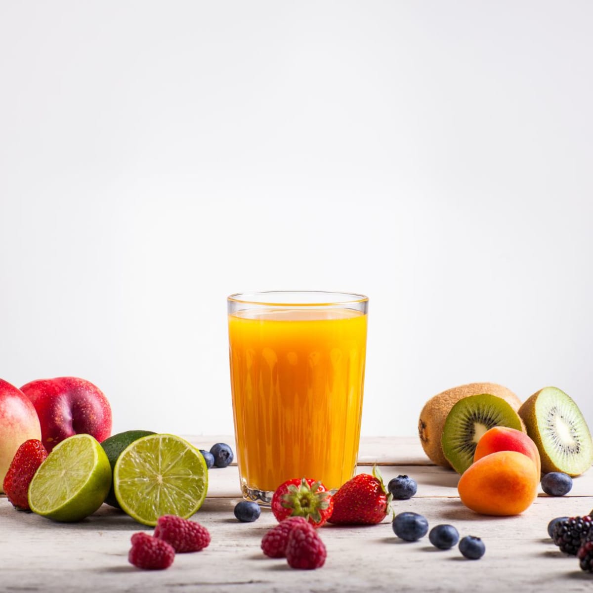 Verre de jus d'orange pour le matin à côté de fruits frais coupés comme des kiwis et myrtilles