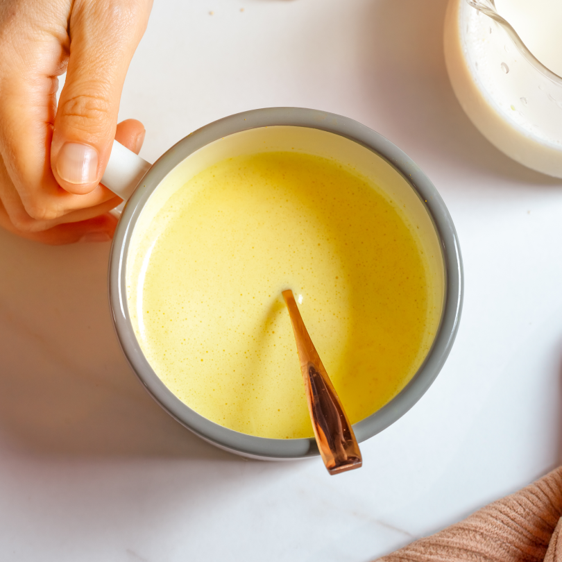 Mug de lait d'or maison pour le petit-déjeuner, tenue par la main d'une jeune femme