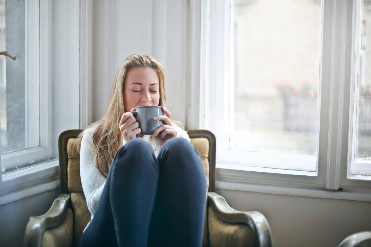 Jeune femme sur un fauteuil, qui profite d'un moment de calme avec une boisson chaude