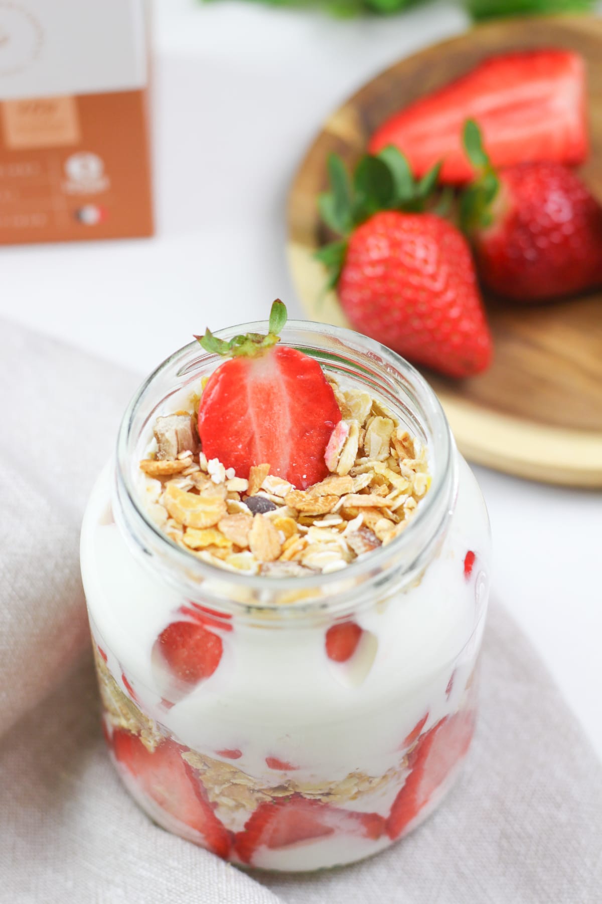 Jarre de muesli sur une base yaourt végétal avec de la fraise, à côté d'un plat de fraises