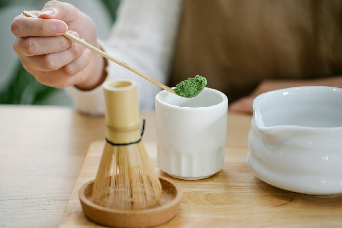 Cuillère de poudre de matcha au-dessus d’une tasse, avec un fouet en bambou (chasen) posé à côté