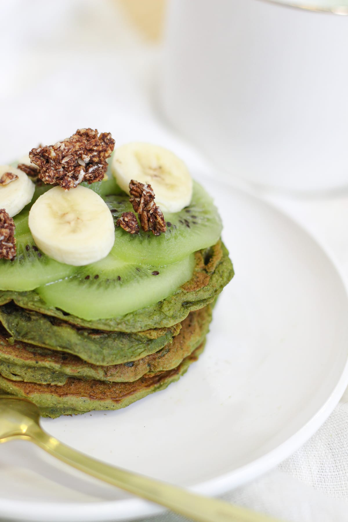 Pile de pancakes verts au matcha et à la banane, avec une banane en tranche et du granola en topping