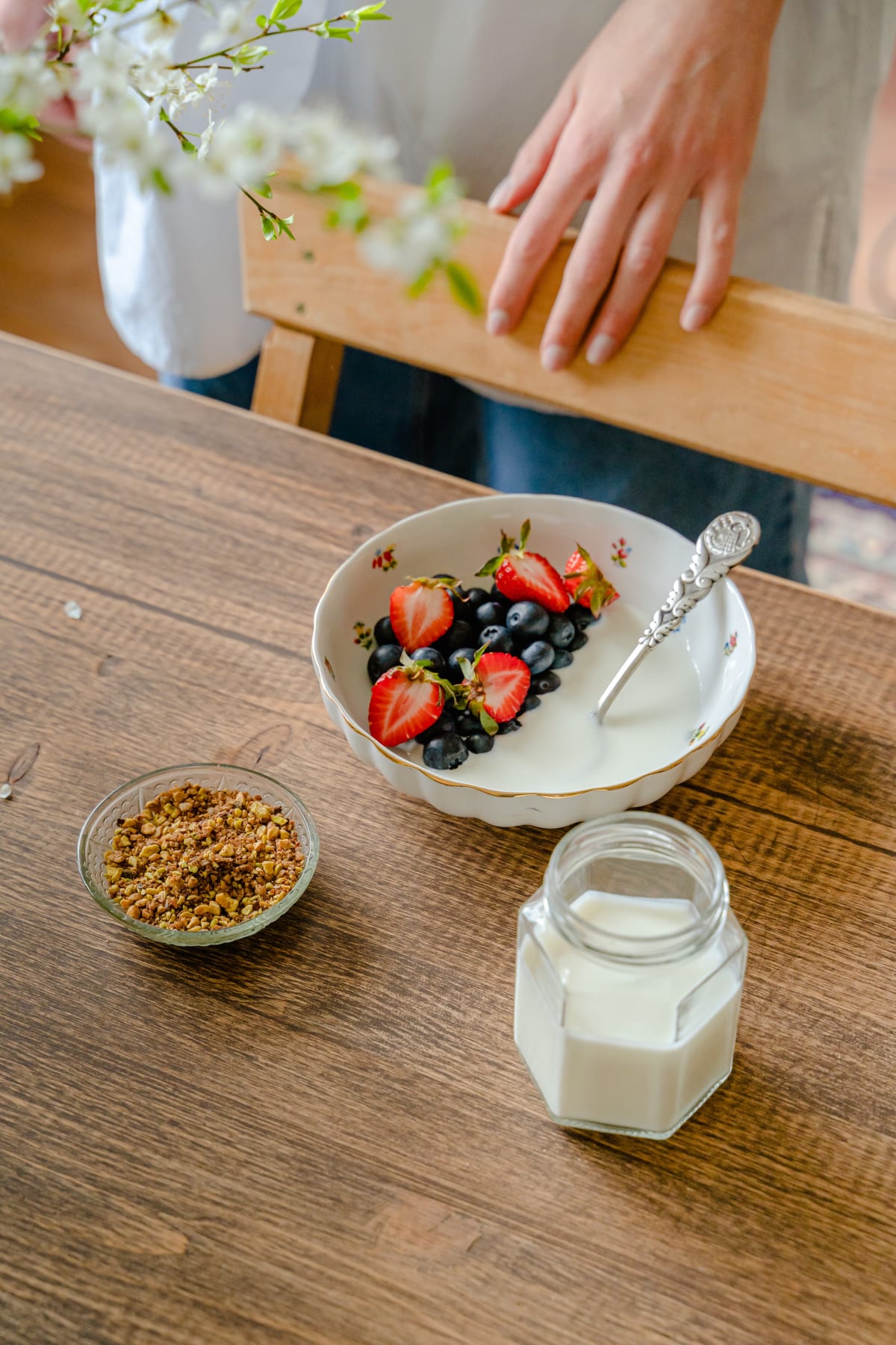 Table avec un bol de granola aux fruits frais, un petit ramequin de toppings et un verre de lait végétal