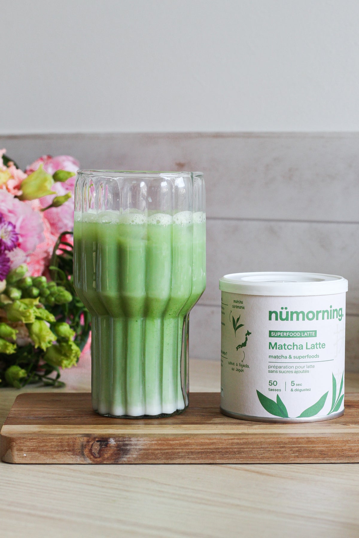 Gros plan sur un verre de matcha latte glacé à côté d'une boite de mélange pour matcha latte