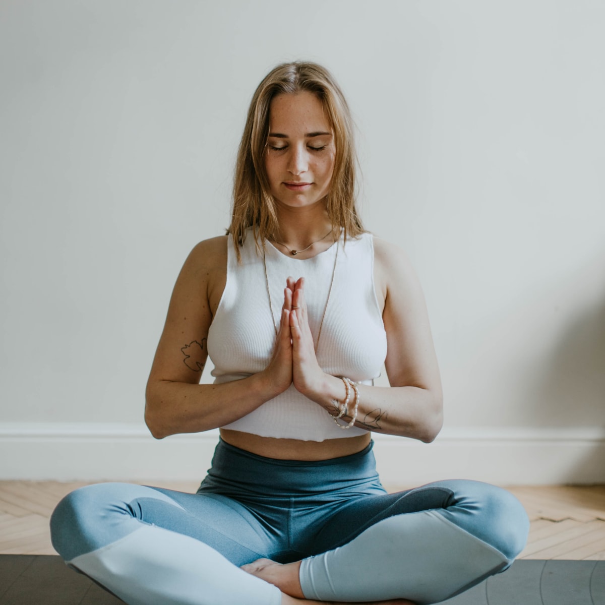 Jeune femme pratique de yoga, assise en tailleur sur son tapis, les mains en prière